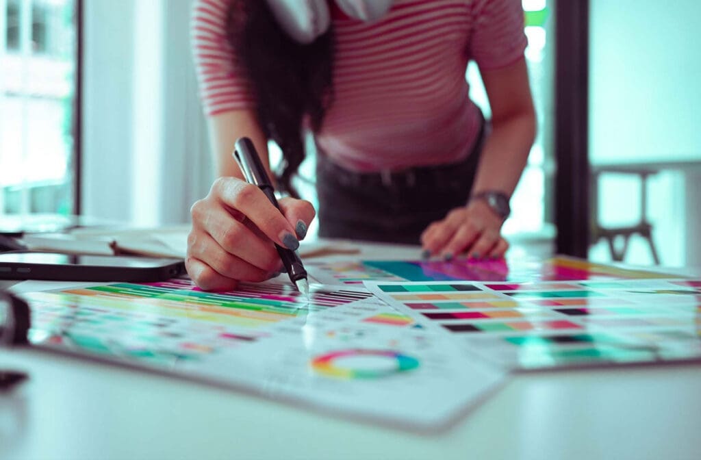 Close-up of a designer’s hand picking colors from a palette while holding a marker.