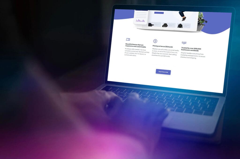 Hands rest on a laptop keyboard as a glowing screen displays a “Start free trial” button, bathed in subtle cyan-magenta lighting.